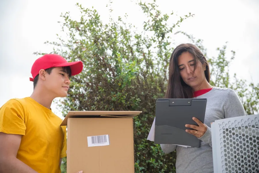 Mover holding a labeled box next to a woman checking a clipboard