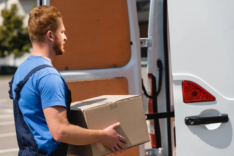 Mover carrying a box next to the open door of a white van