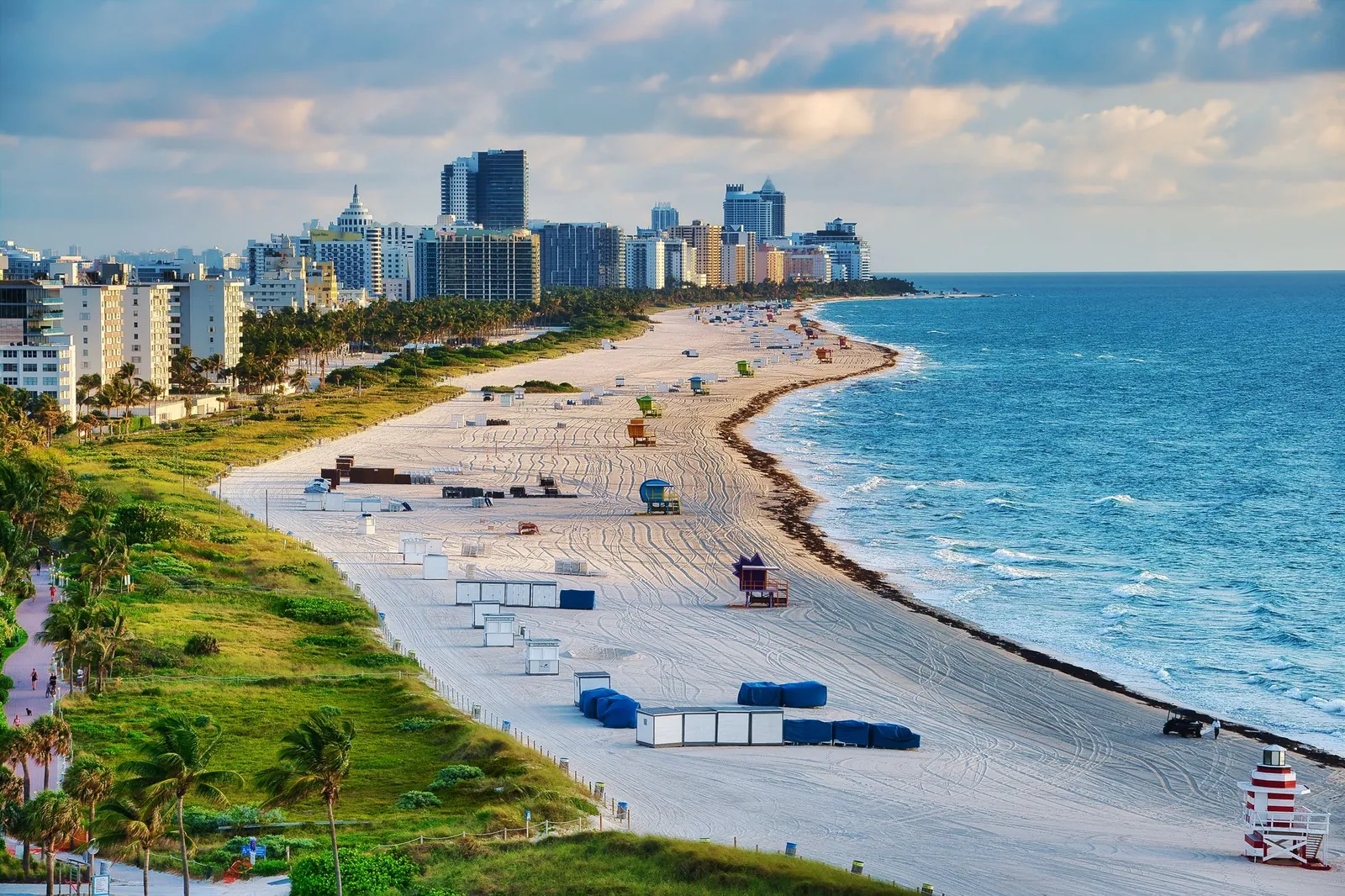 Elevated view of Miami Beach: long white-sand beach with lifeguard towers and cabanas, turquoise ocean, dunes with palms and a line of high-